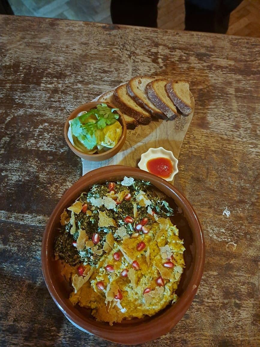 Roast squash in a terracotta dish topped with pomegranate seeds, shaved cheese and herbs, with bread alongside