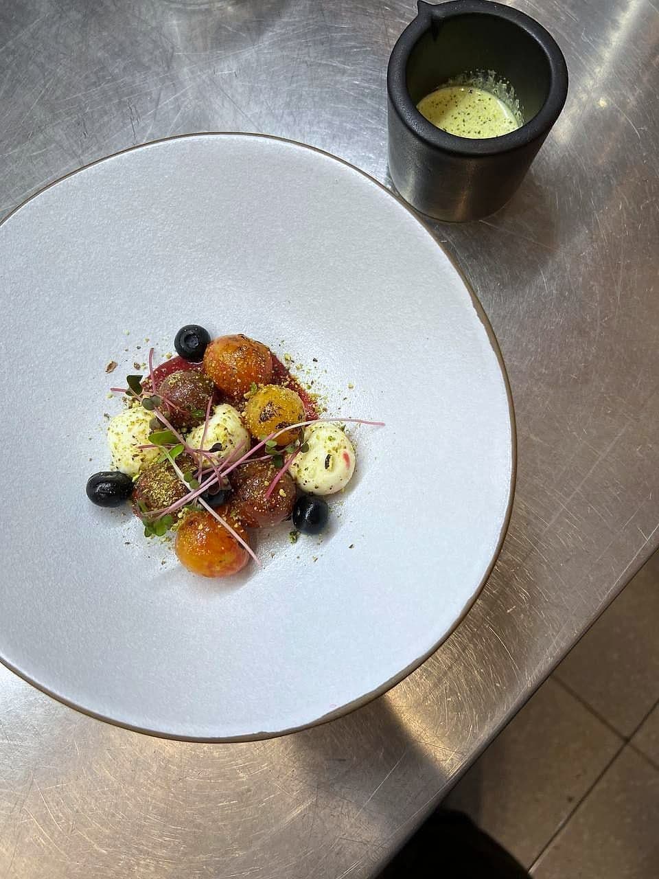 Heritage tomatoes with small mozzarella, black olives and micro basil on a white plate