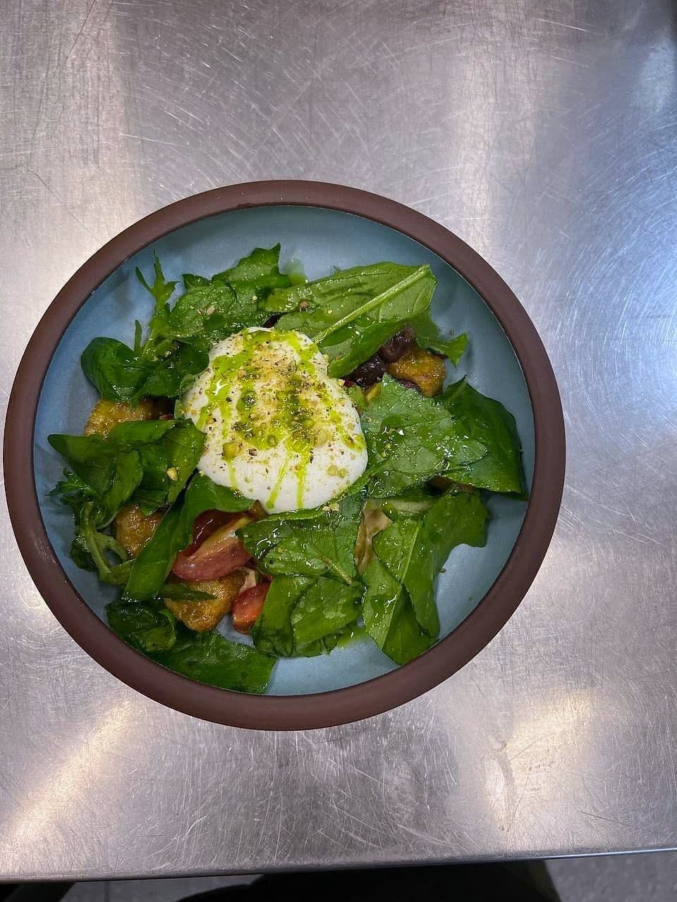 Whole burrata on dressed green leaves with tomato and croutons in a blue-glazed bowl