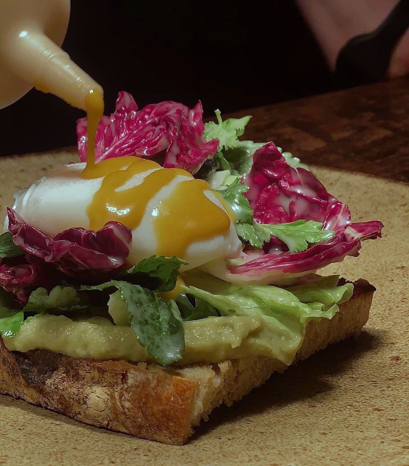 Poached egg on thick toasted sourdough with hollandaise being poured over, radicchio and green leaves