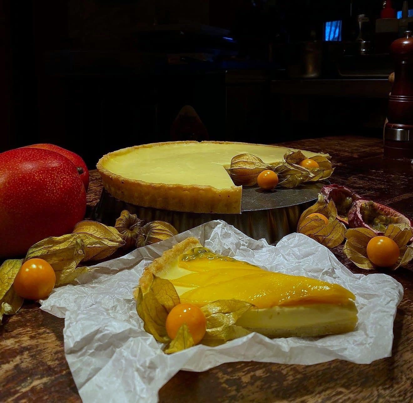 A baked cheesecake and a slice of mango tart on parchment, with physalis and pomegranate around them
