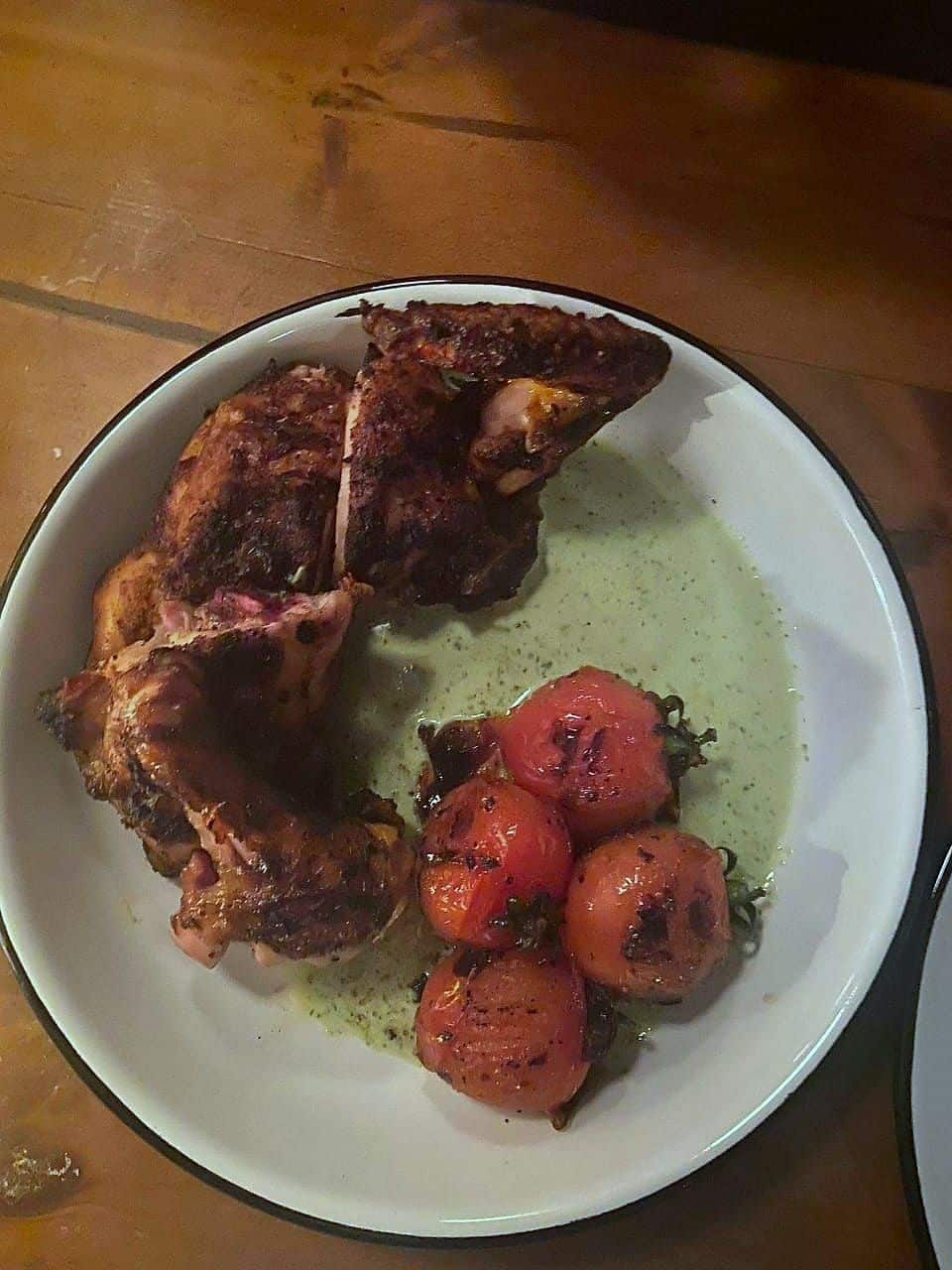 Roasted split poussin with blistered cherry tomatoes in a green herb butter, in a white bowl