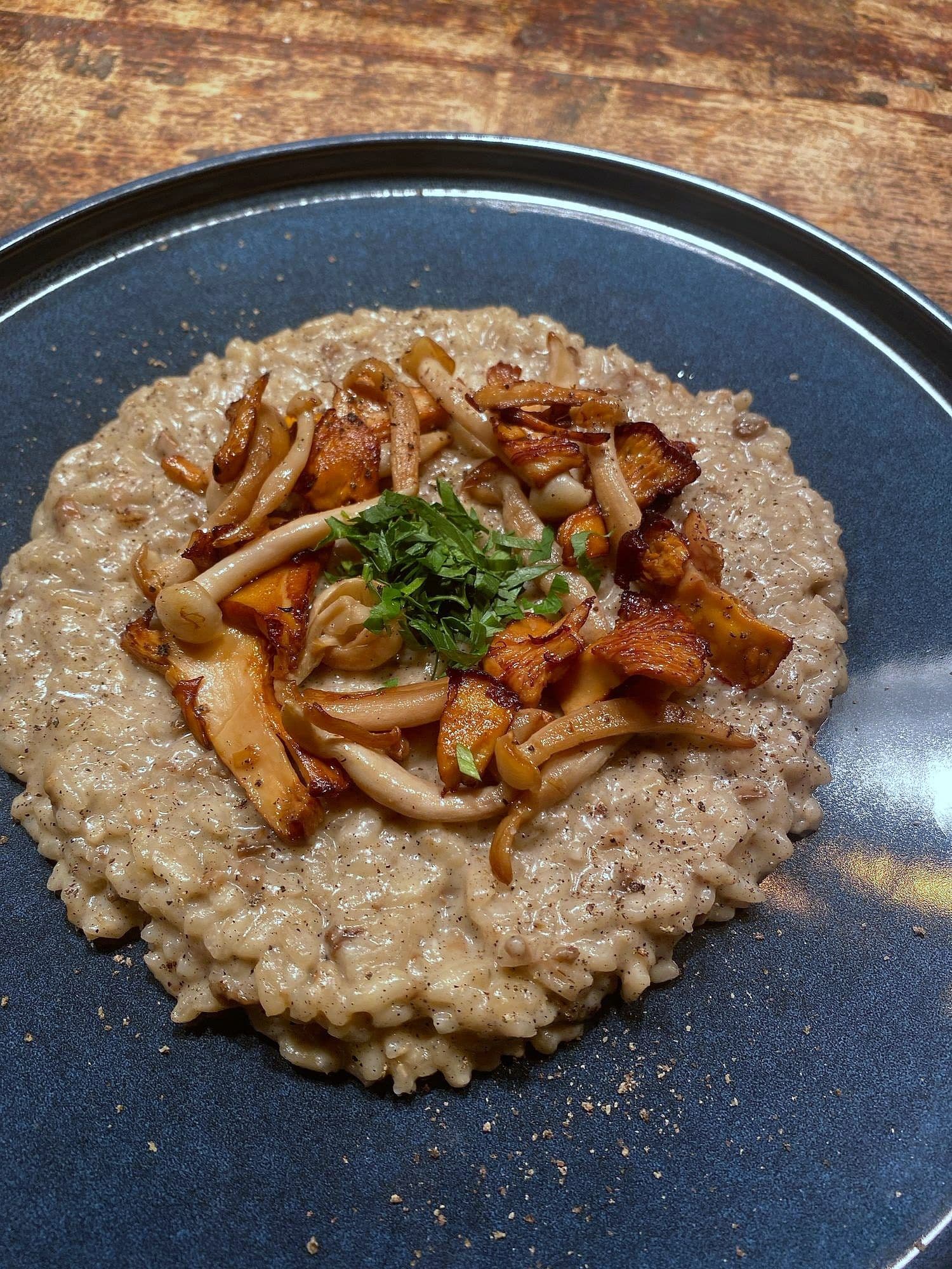 Mushroom risotto on a blue plate topped with sautéed shimeji mushrooms and herb oil