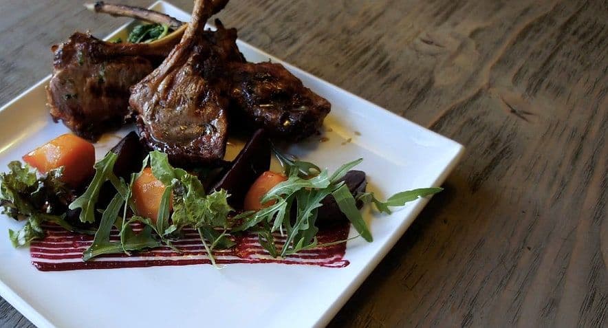 Grilled lamb chops standing on roast root vegetables with rocket on a square white plate