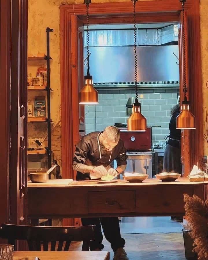 Chef plating at a restaurant pass under copper heat lamps