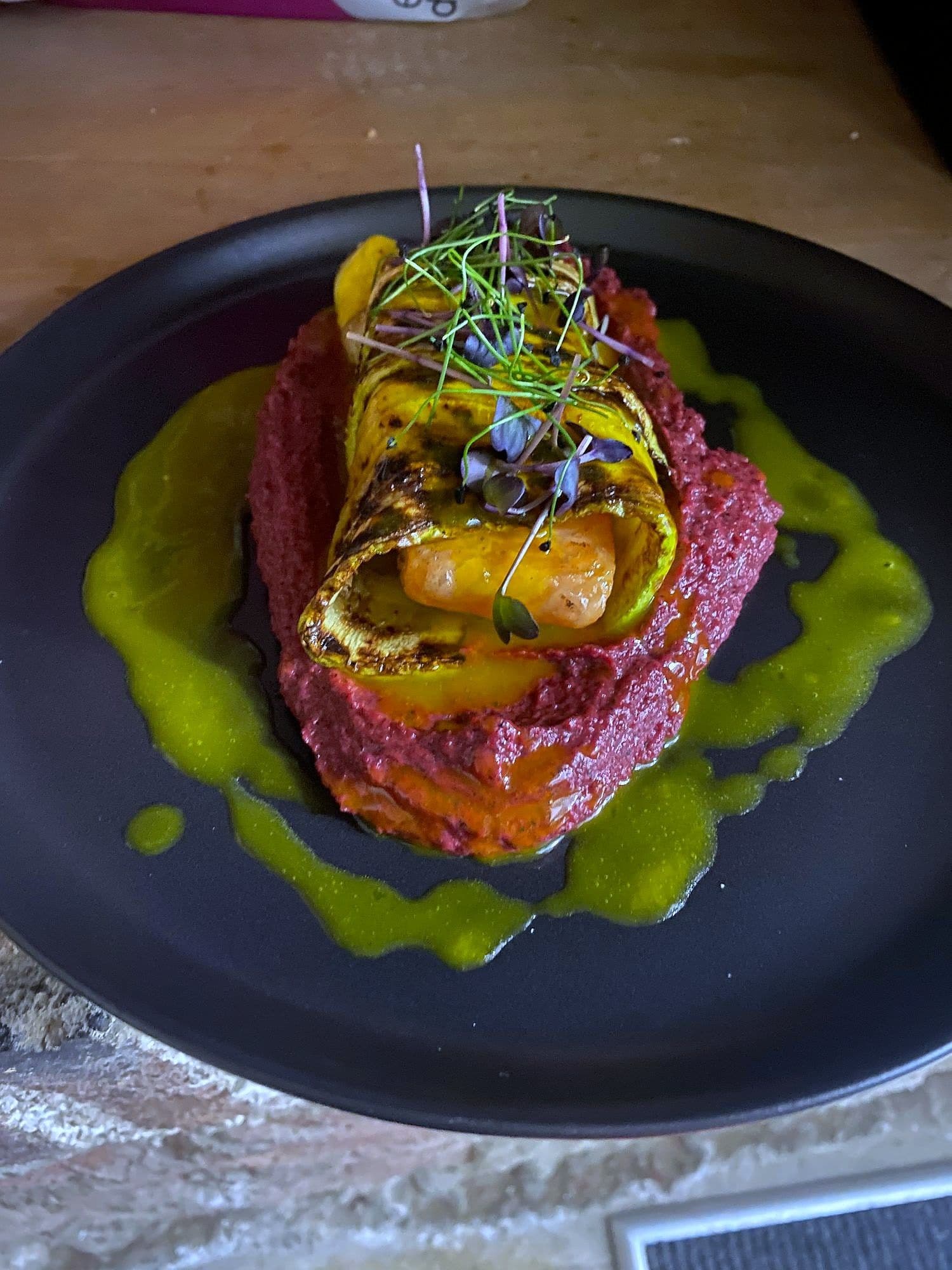 Pressed beetroot tartare topped with grilled peach and micro herbs, ringed by green herb oil on a dark plate