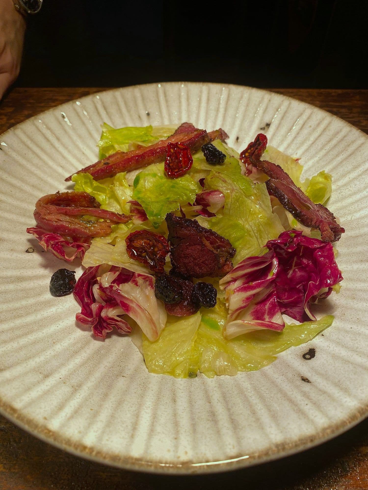 Salad of radicchio and gem lettuce with strips of cured meat and black olives on a fluted plate