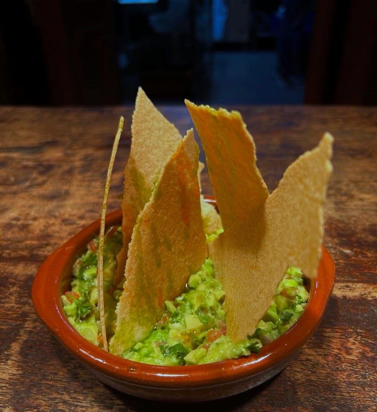 Coarsely crushed guacamole in a red terracotta bowl with tall shards of crisp flatbread standing upright