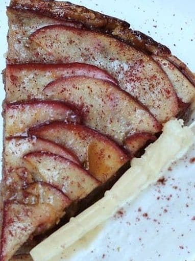 Slice of thin apple tart with fanned apple slices and a quenelle of cream on a white plate