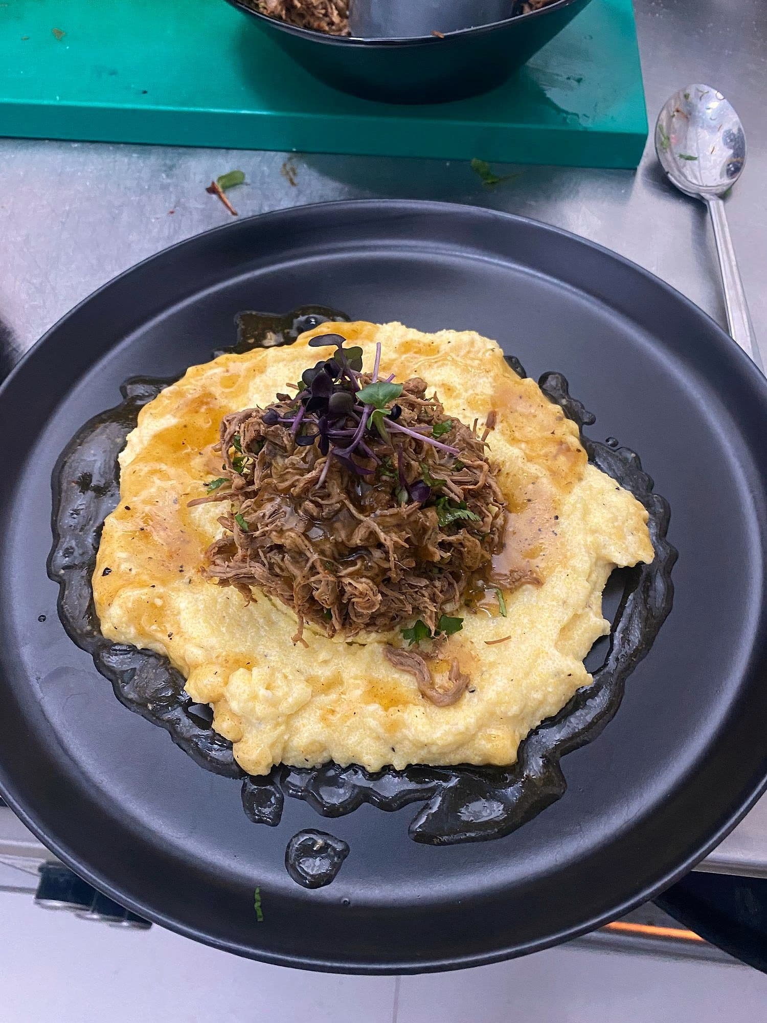 Shredded slow-cooked meat on soft polenta in a heavy black pan