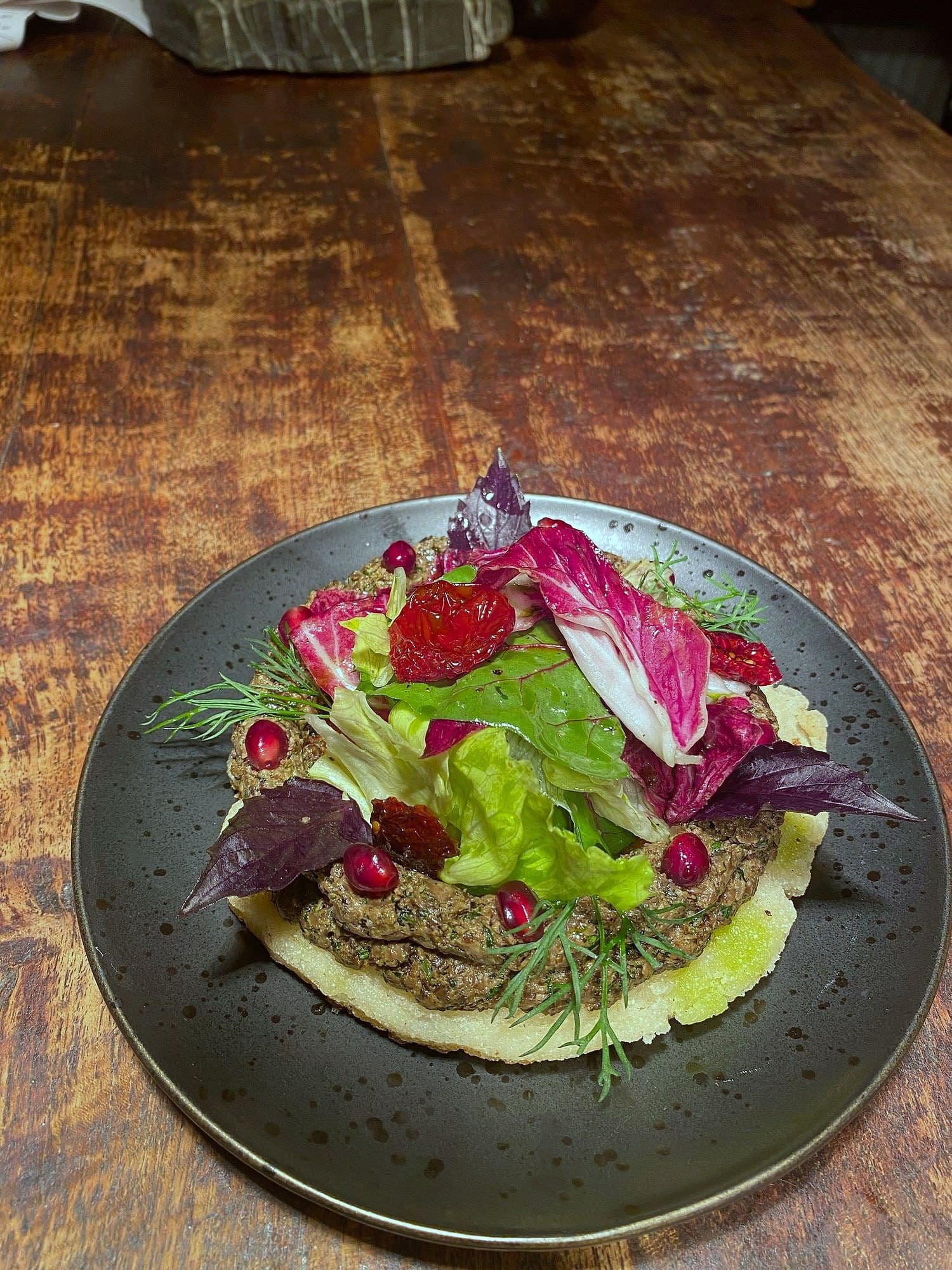 Hand-cut beef tartare on a whipped base with bitter leaves, herbs and redcurrants on a dark plate