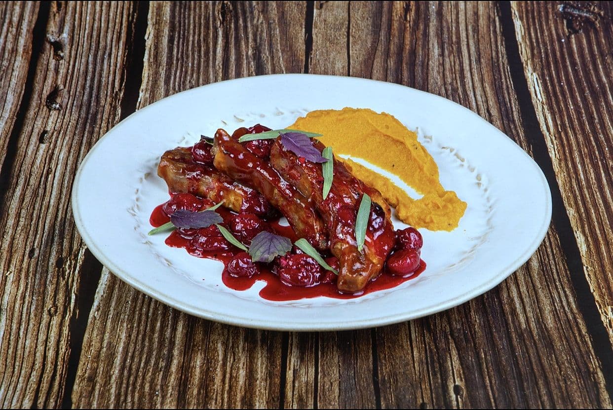 Sticky glazed ribs with a sweep of orange squash purée on a white plate