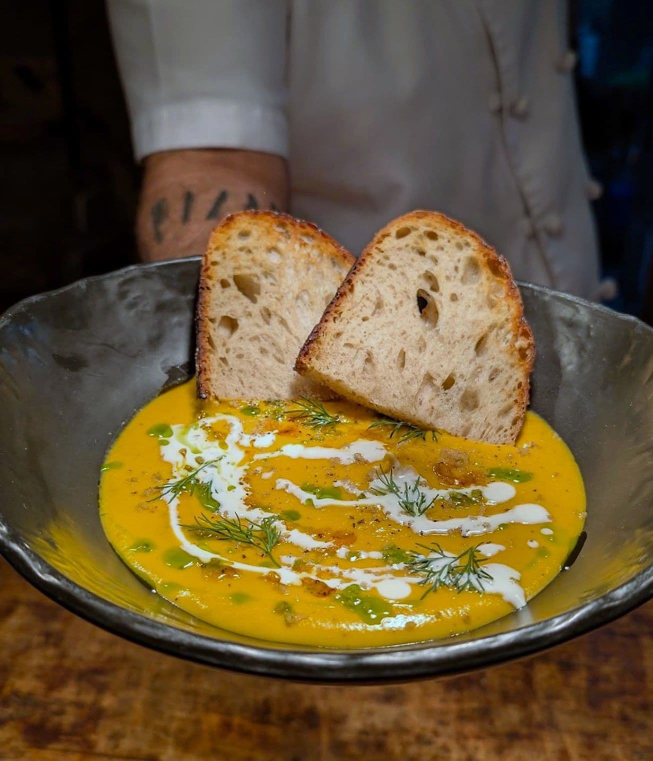 Roast carrot soup in a dark bowl with a swirl of cream and fresh dill, with two slices of sourdough