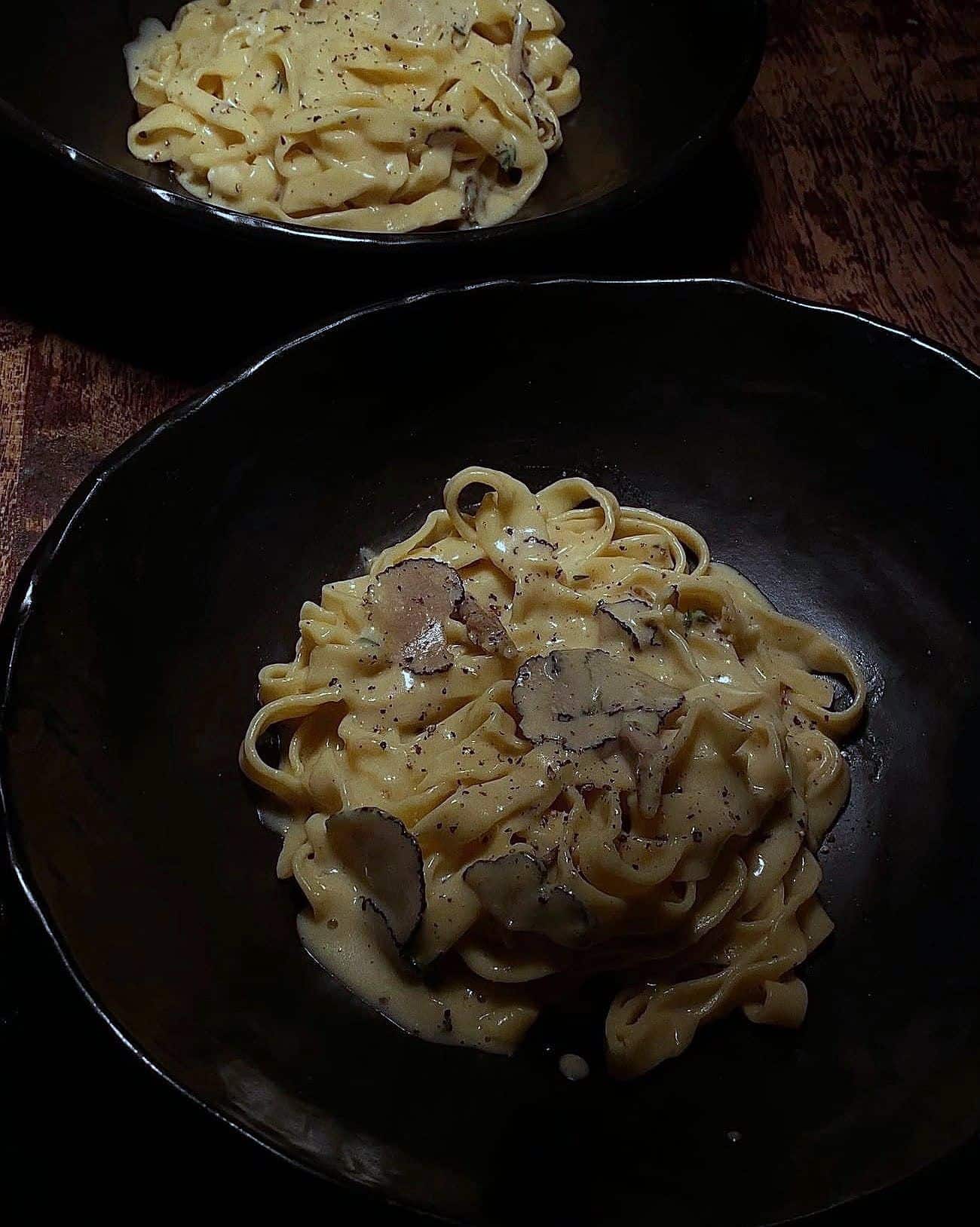 Fresh egg tagliatelle in a cream sauce topped with shaved black truffle, in a black bowl
