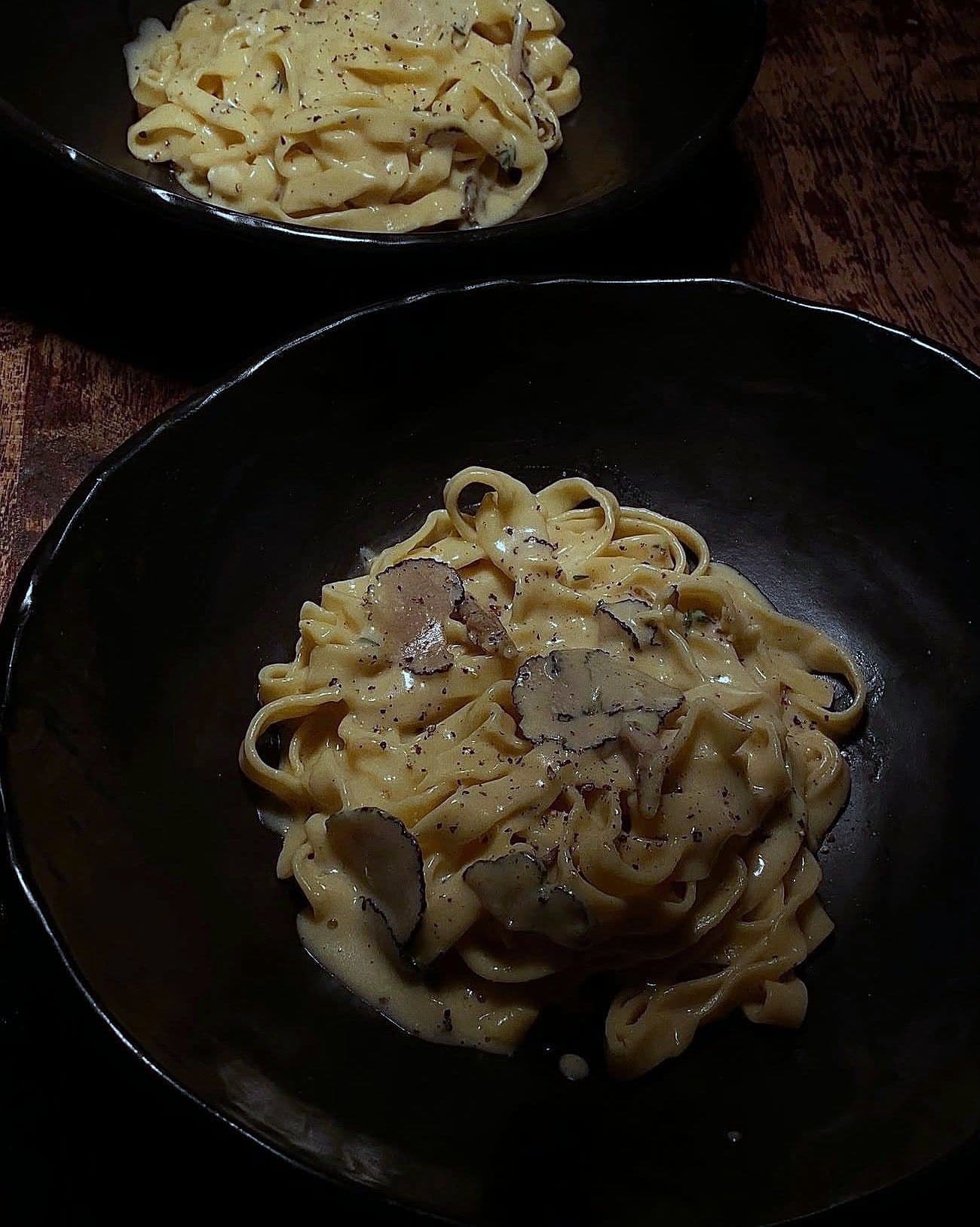 Fresh egg tagliatelle in a cream sauce topped with shaved black truffle, in a black bowl