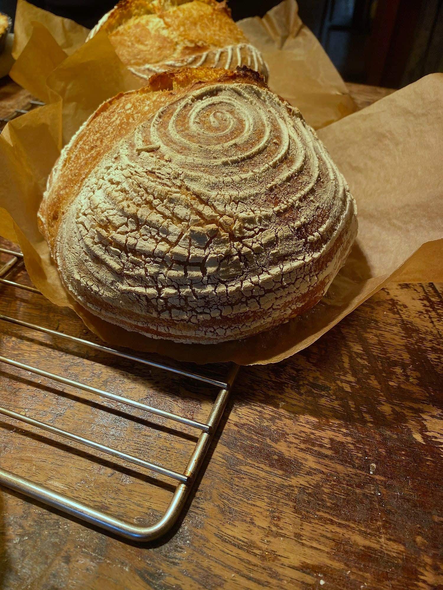 Round sourdough boule with spiral score pattern and blistered crust, cooling on a wire rack