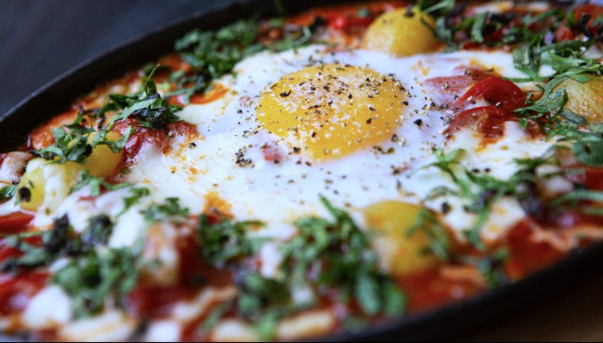 Shakshuka with baked eggs in a spiced tomato and pepper sauce, topped with fresh herbs, in a black pan