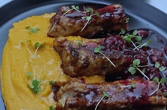Glazed ribs on a bed of orange squash purée topped with micro herbs