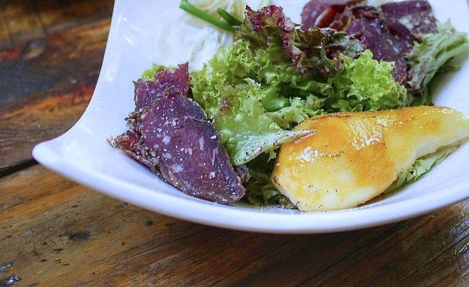 Salad of mixed and purple leaves with roast squash wedges and soft cheese on a white plate