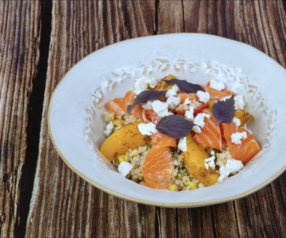 Bowl of quinoa with cured salmon, orange segments, crumbled feta and purple basil on a wooden table