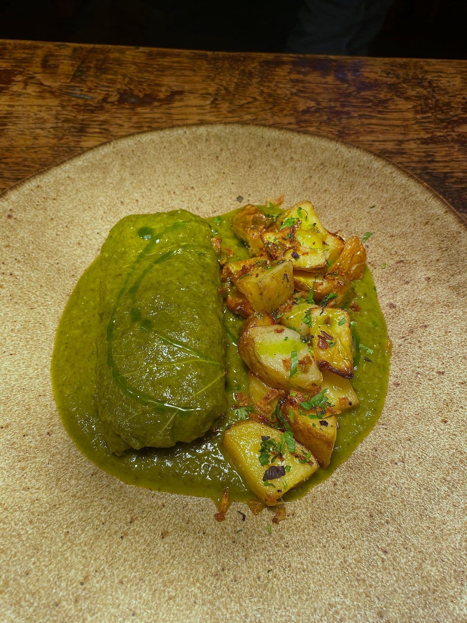 Bright green pea and herb purée beside crushed roast potatoes on a stoneware plate