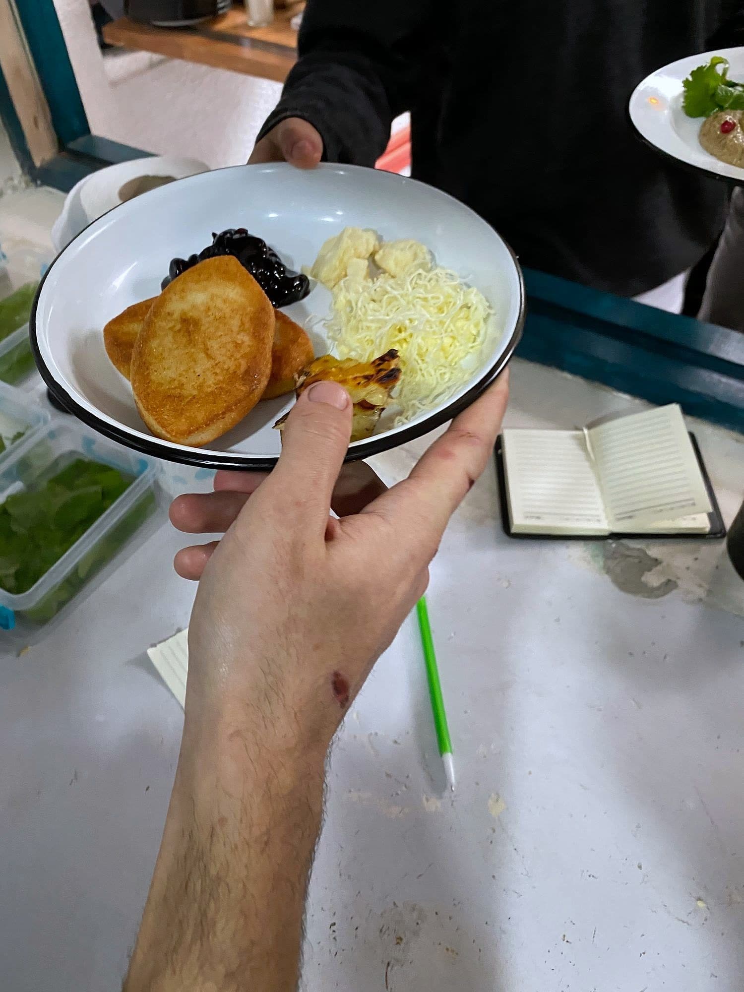 A hand holding a white bowl containing fried bread, grated cheese and confit garnish in a development kitchen