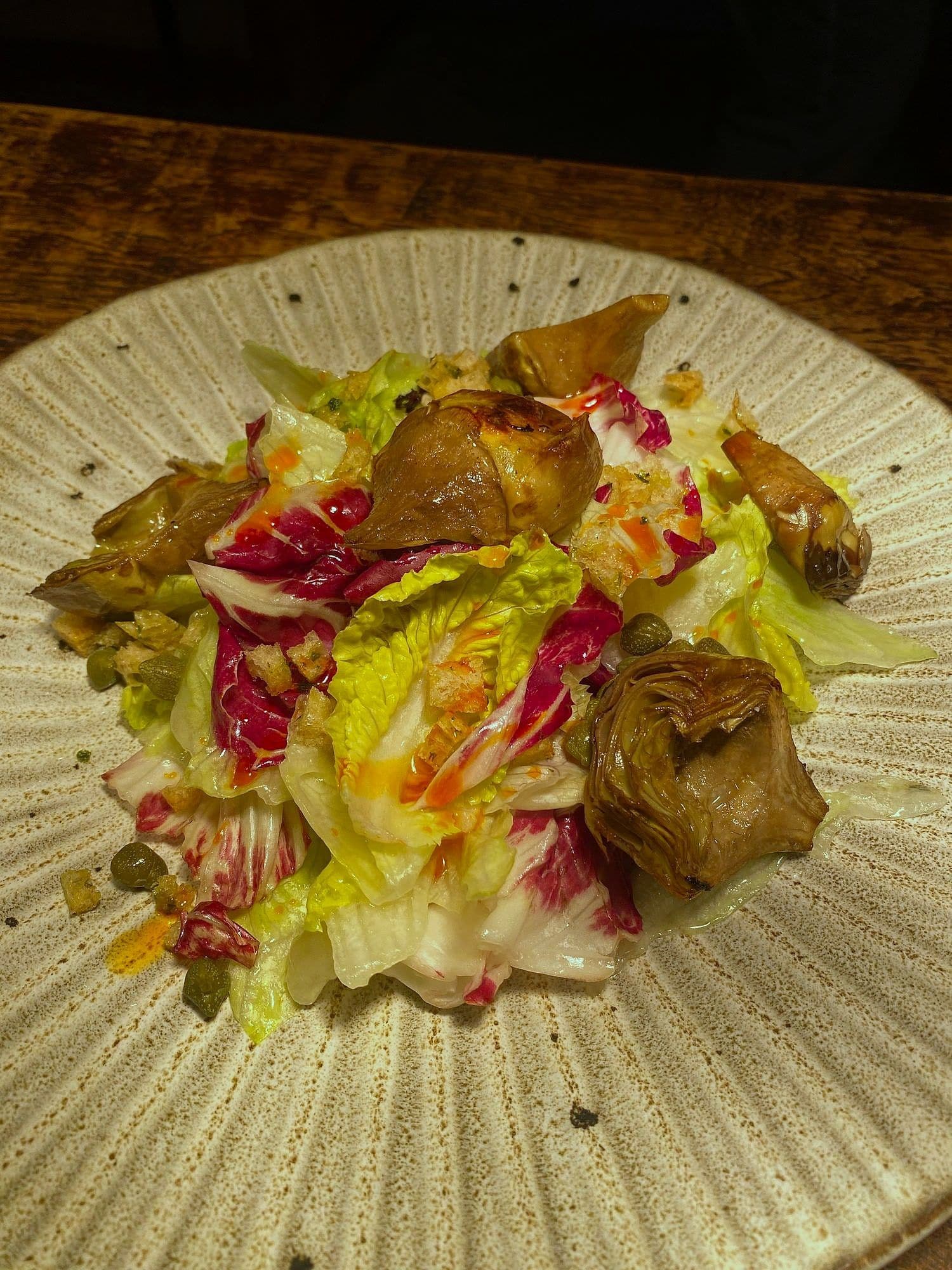 Salad of braised artichoke hearts, radicchio, gem lettuce and capers on a fluted plate