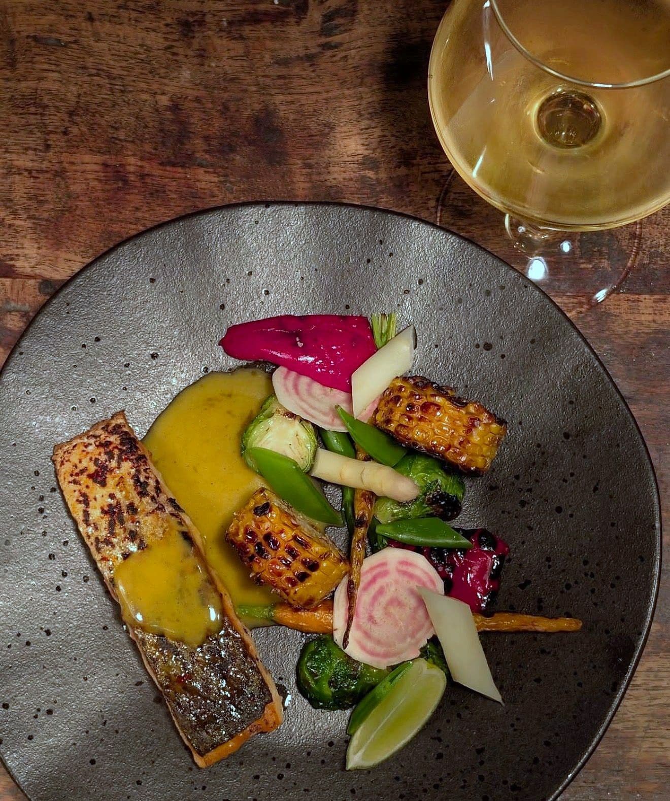 Salmon fillet on corn purée with charred corn, pickled beetroot, courgette and radish on a dark plate