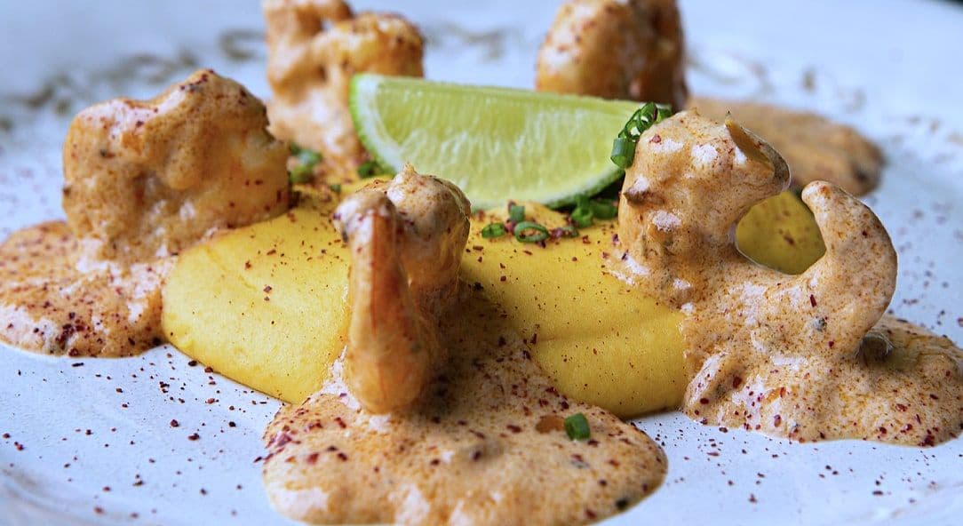 Fried polenta pieces with spiced cream sauce, coriander and a lime wedge on a white plate