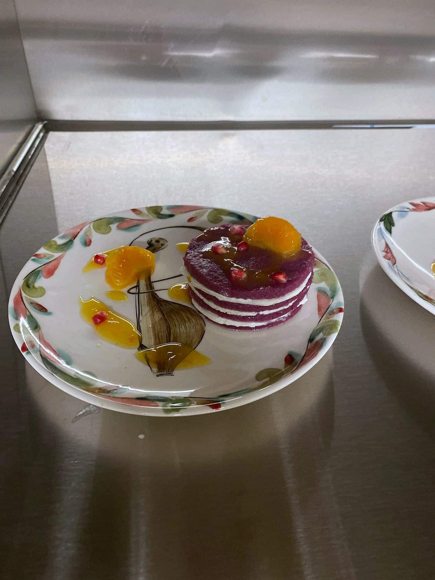 Stacked beetroot discs with citrus segments and dill oil on a floral-rimmed plate