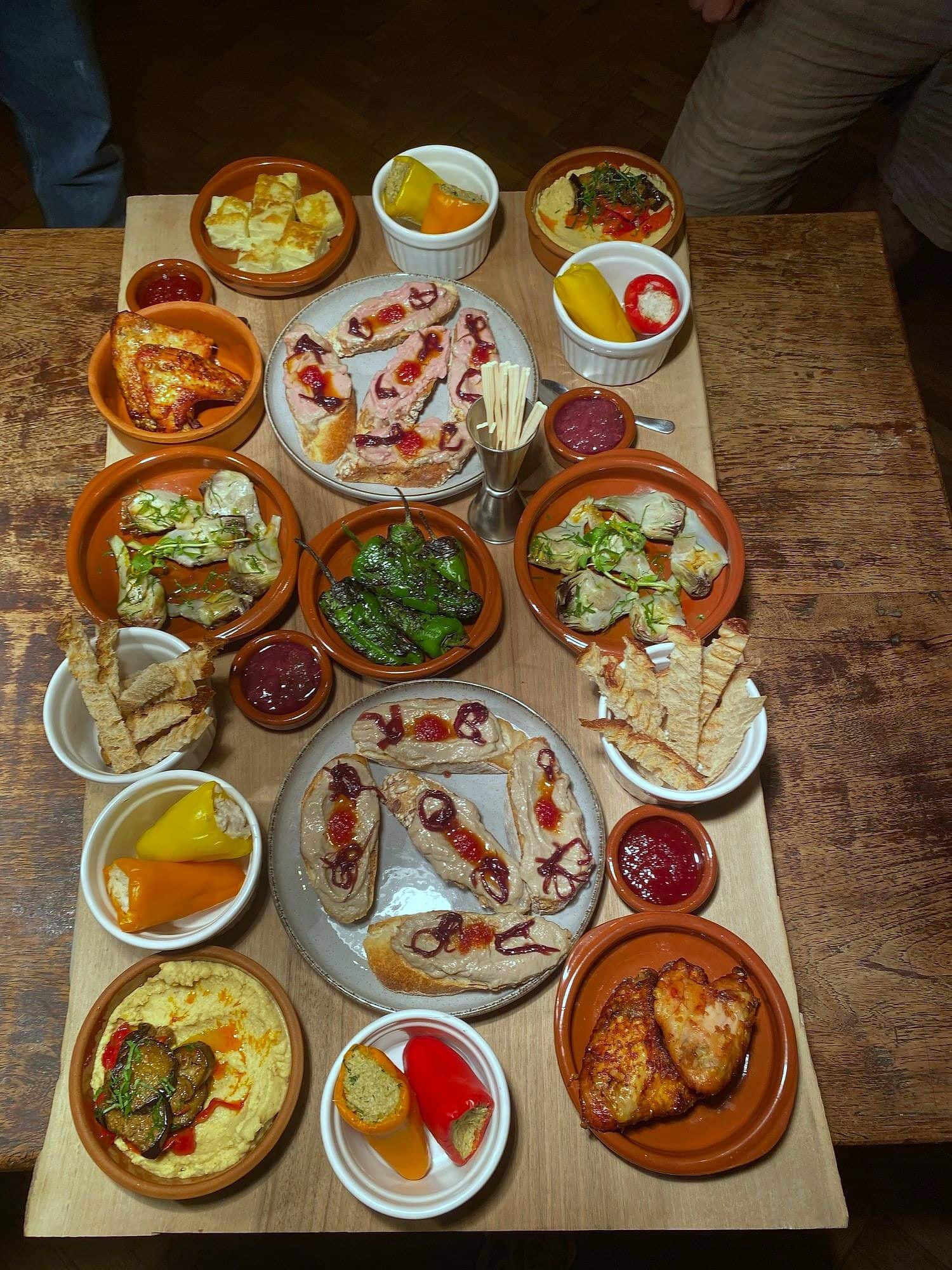 Large wooden board covered with terracotta dishes of dips, pickles, grilled vegetables, cured fish and flatbread