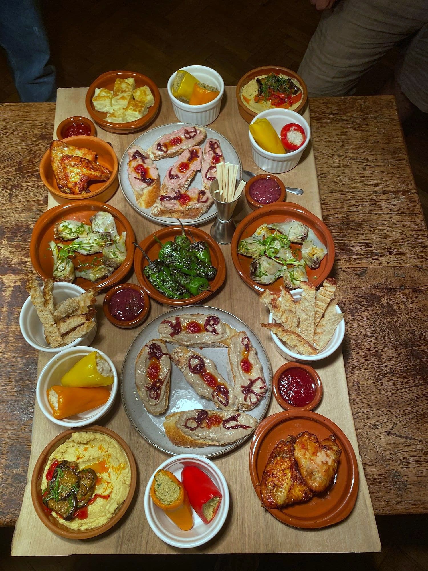Large wooden board covered with terracotta dishes of dips, pickles, grilled vegetables, cured fish and flatbread