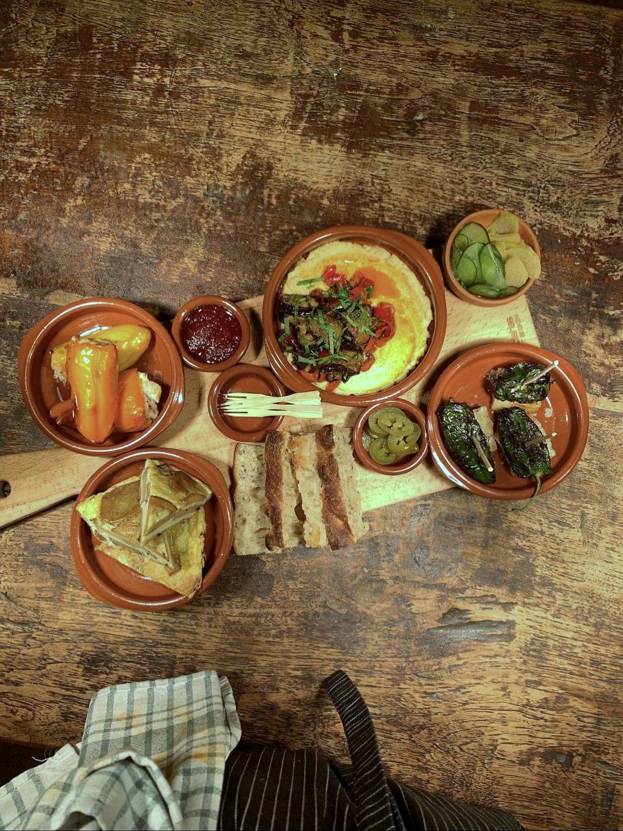Overhead view of a wooden table set with terracotta dishes of dips, pickles and grilled vegetables