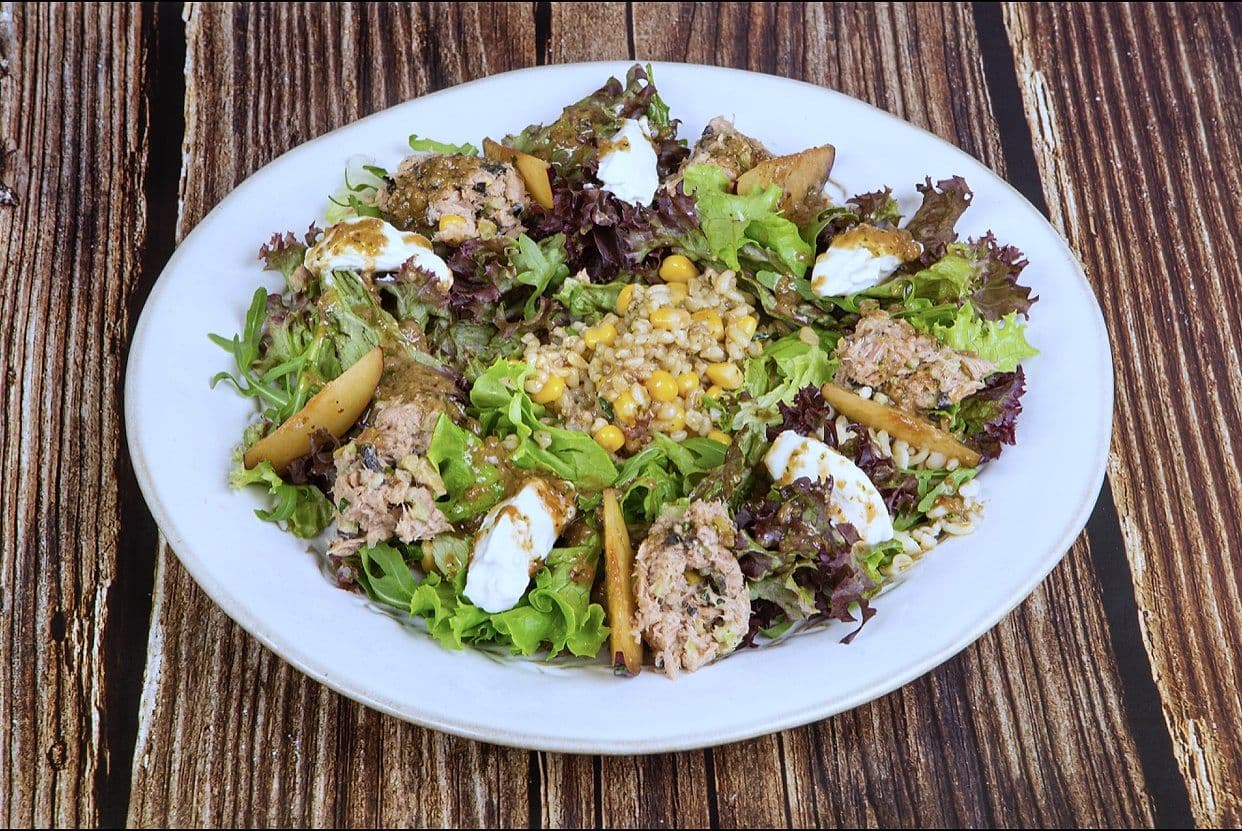 Warm salad of mixed leaves, grains, sweetcorn, goat cheese and roasted vegetables on a white plate