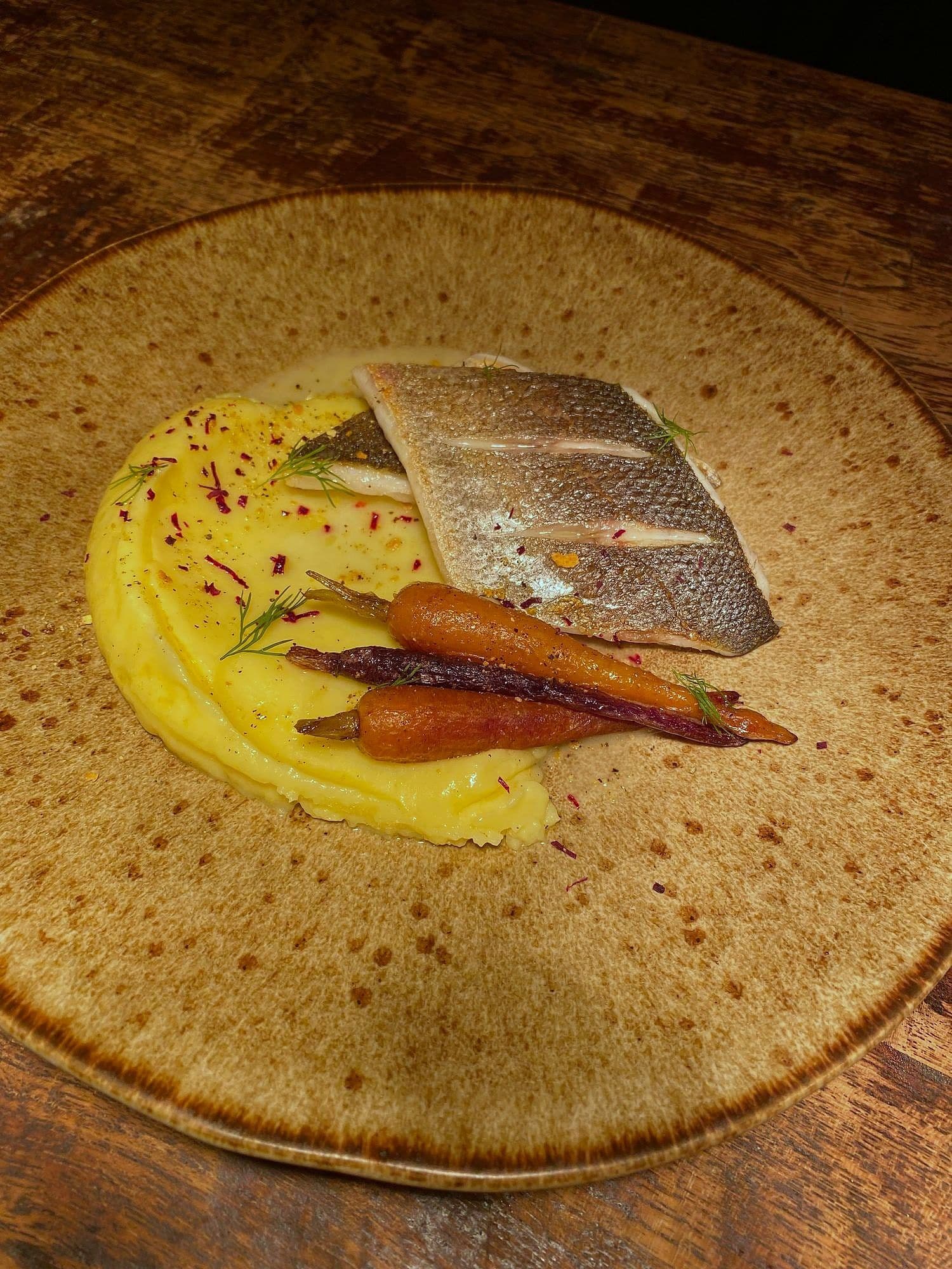 Crisp-skinned sea bass on a saffron-yellow purée with two glazed baby carrots on a stoneware plate