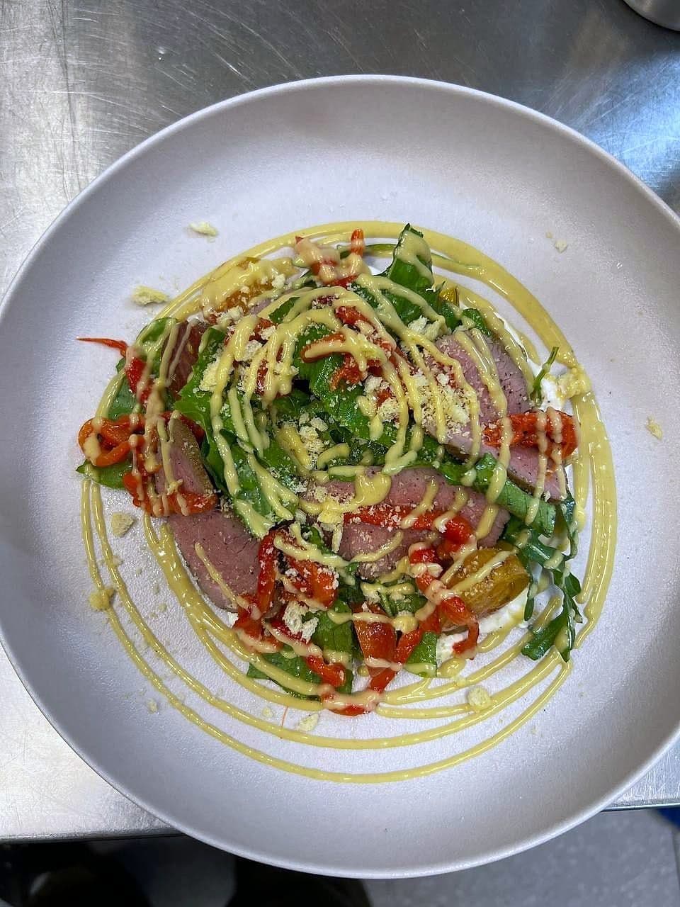 Slices of seared tuna with avocado, red chilli and herb dressing drawn in circles on a white plate