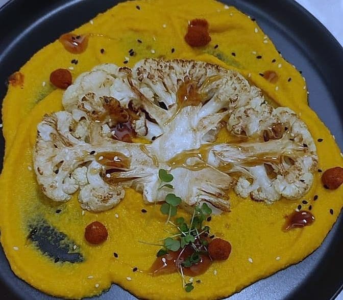 Roasted cauliflower steak on a bright yellow turmeric purée with chilli oil dots and micro herbs