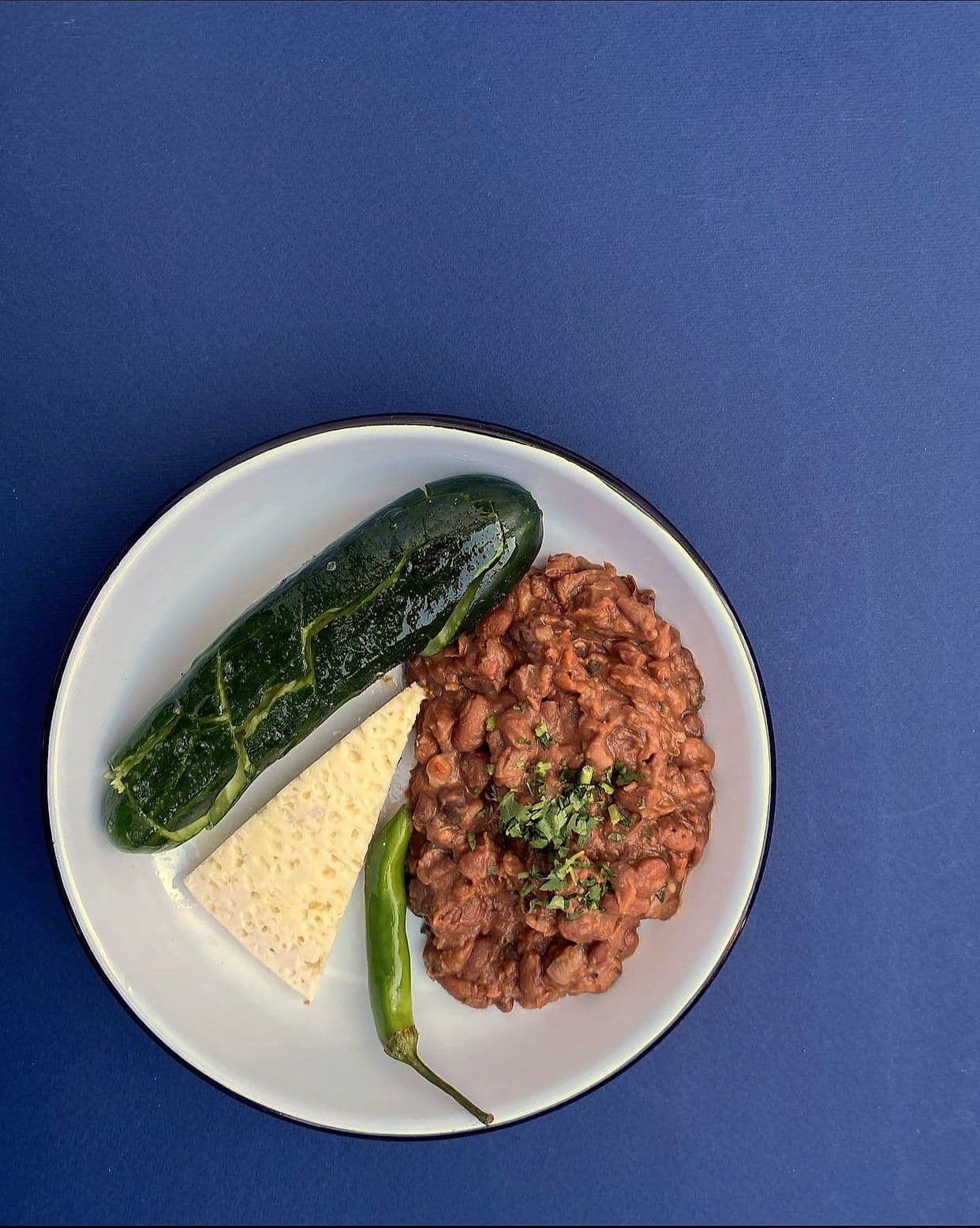 Beef tartare with a whole charred green pepper and grated cheese on a white plate against a blue background