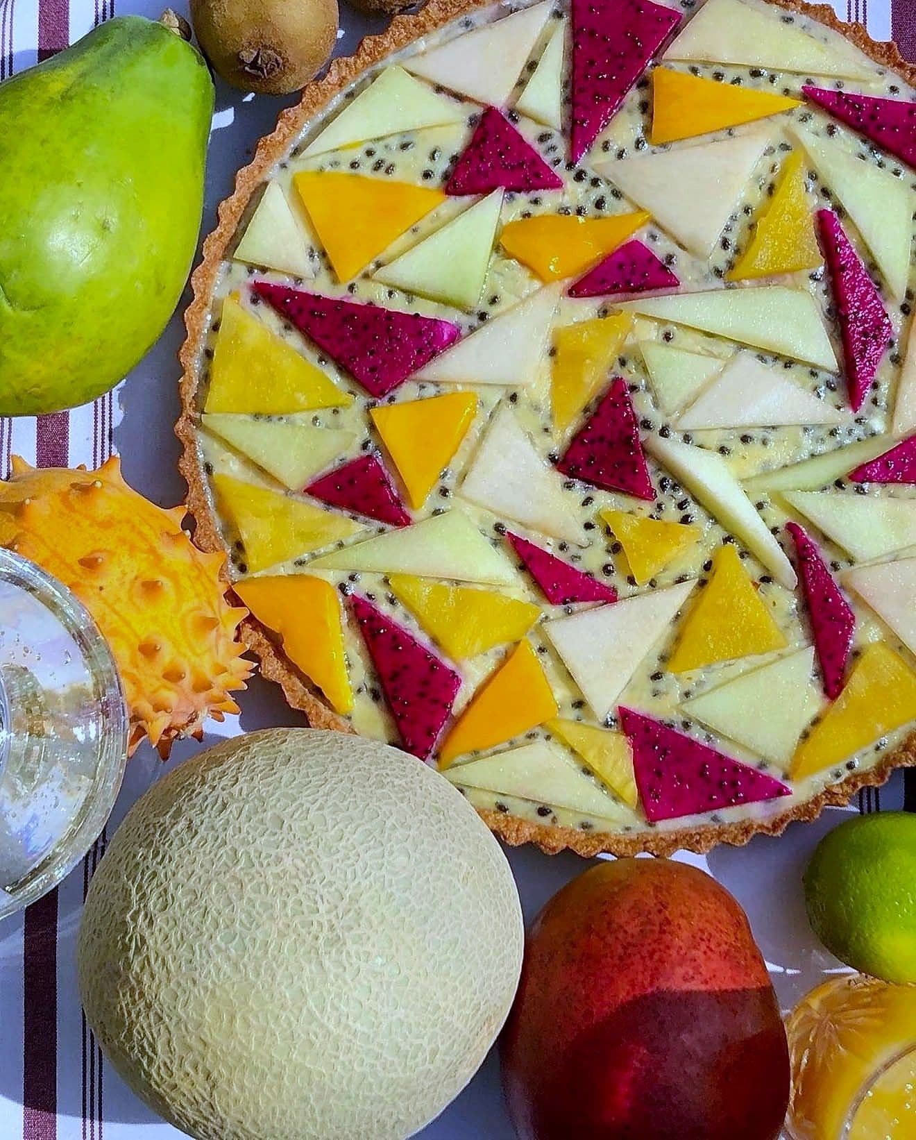 Tart topped with mango, dragon fruit and melon cut into triangles in a geometric pattern, with whole fruit alongside