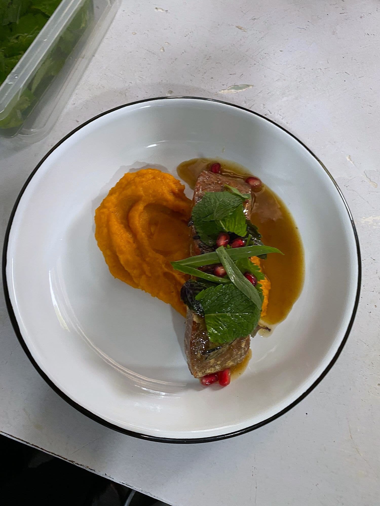 Sliced pink duck on orange squash purée with dark jus, pomegranate seeds and herbs on a white plate