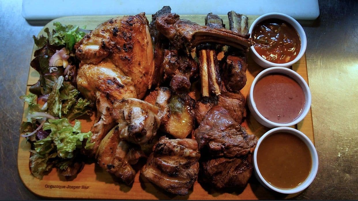 Wooden board of mixed grilled meats with three dipping sauces and dressed leaves